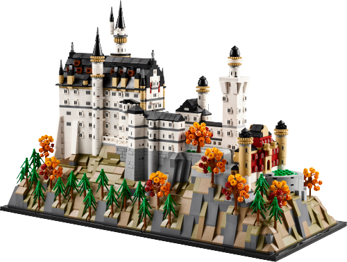 Visuel officiel du château LEGO Neuschwanstein 21063 : grands bâtiments blancs, toits sombres et tourelles à anneaux beiges sur un relief rocheux gris et beige, avec conifères verts, arbres d’automne et entrée rouge sombre, sur socle noir.
