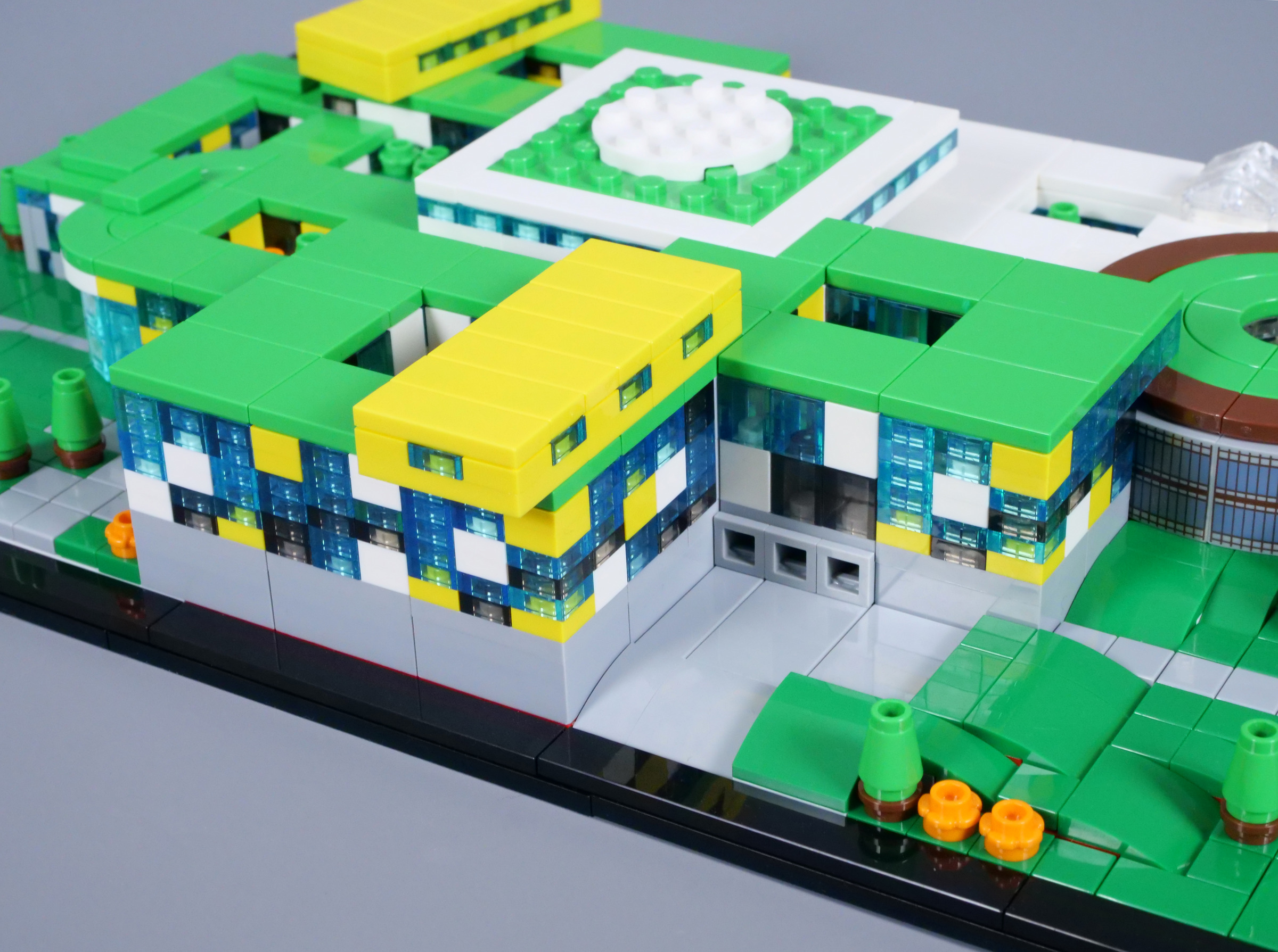 Photographie Brickset des façades du Campus, avec petites plaques bleues translucides entre éléments blancs et jaunes, toits verts, volume jaune en hauteur et trois petites ouvertures carrées grises au niveau inférieur.